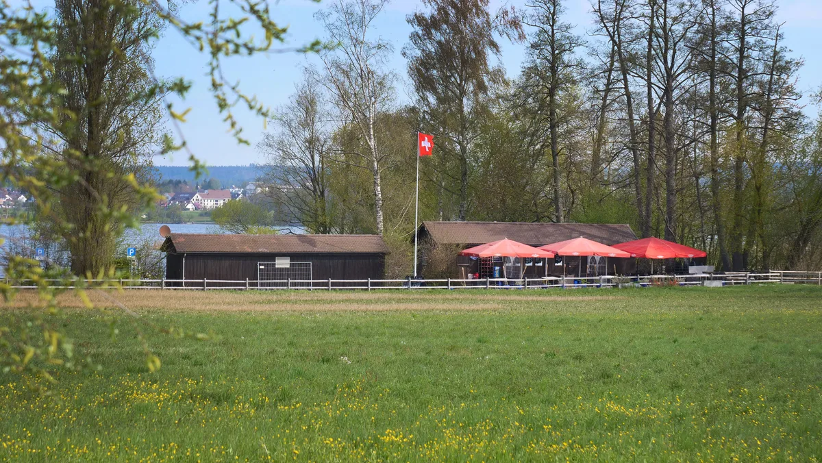 Baracken, eine Wiese und eine Schweizer Fahne am Greifensee.